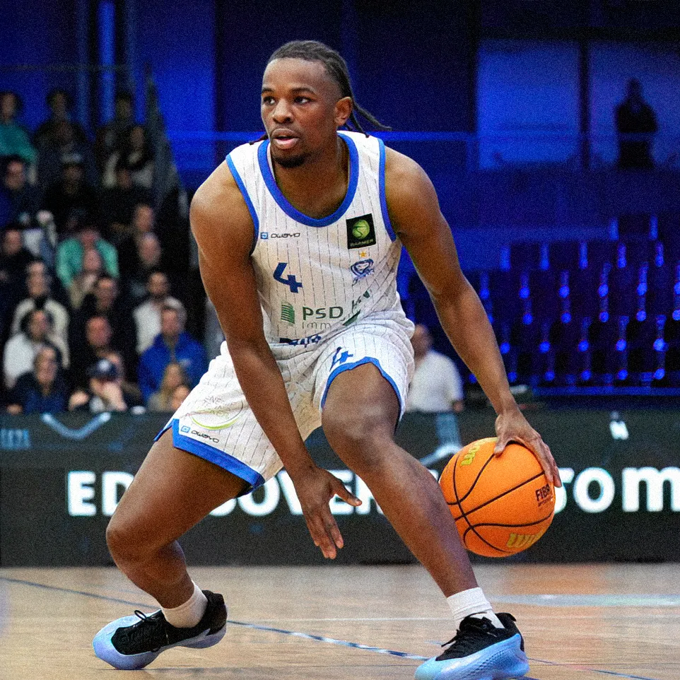 A basketball player dribbles the ball on the court while wearing a striped jersey with the number 4.